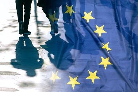 Menschen und Schatten hinter EU-Flagge.