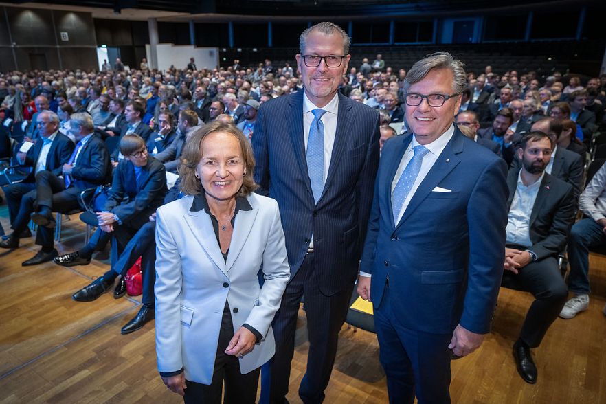Drei Personen vor gro&szlig;em Publikum in der Stadthalle.