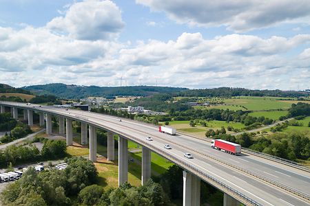 Autobahnbr&uuml;cke mit LKWs und Autos vor gr&uuml;ner Landschaft.