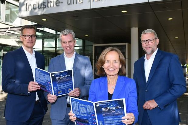Vier Personen vor der Industrie- und Handelskammer halten Brosch&uuml;ren hoch.