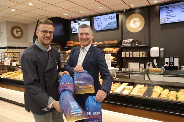 Zwei M&auml;nner in einer B&auml;ckerei halten Brott&uuml;ten mit Ausbildungswerbung in der Hand.
