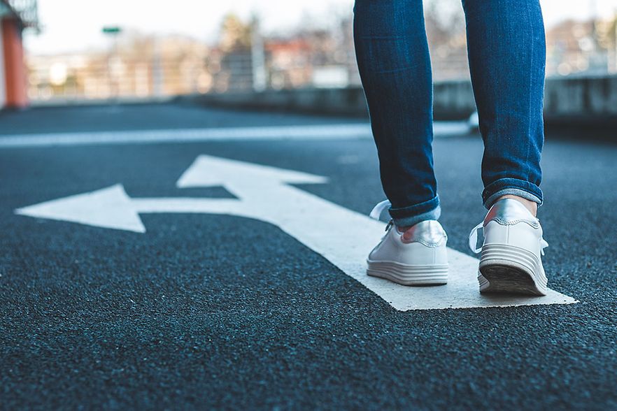 Make decision which way to go. Walking on directional sign on asphalt road.