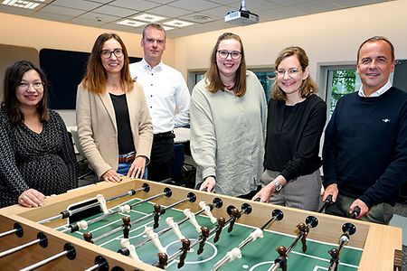 Sechs Personen stehen um einen Tischkicker in einem Besprechungsraum.