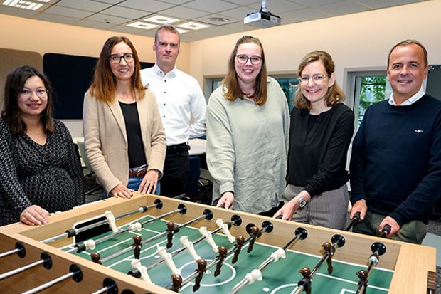 Sechs Personen stehen um einen Tischkicker in einem Besprechungsraum.