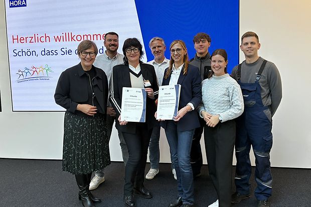 Eine Gruppe von Menschen steht zusammen. Zwei Personen in der Mitte halten Zertifikate zur gerade geschlossenen Kooperation