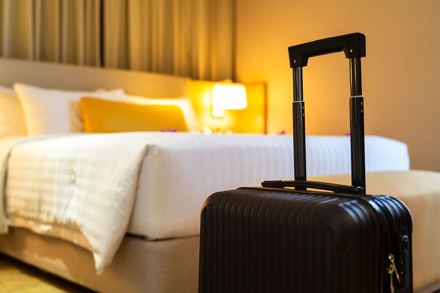 Koffer steht in einem gem&uuml;tlich beleuchteten Hotelzimmer vor einem frisch gemachten Bett