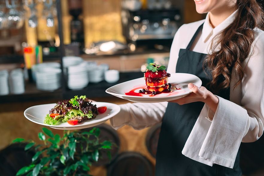 Eine Kellnerin serviert zwei Teller mit Salat und einem Dessert in einem Restaurant.