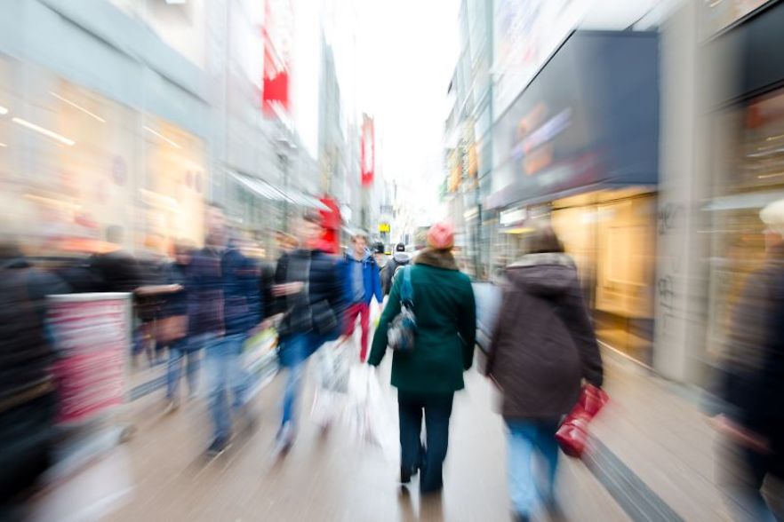 Belebte Einkaufsstra&szlig;e mit vielen Passanten in Bewegung, unscharf dargestellt f&uuml;r einen Dynamikeffekt.