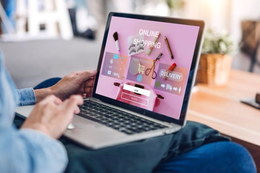 Person nutzt ein Laptop, auf dessen Bildschirm eine bunte Online-Shopping-Seite mit Einkaufs- und Liefericons angezeigt wird.