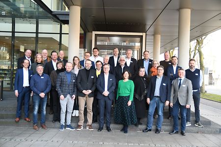 Gruppenfoto von rund 30 Personen, die vor einem Geb&auml;ude der IHK stehen und in die Kamera l&auml;cheln