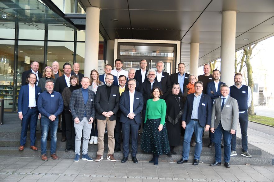 Gruppenfoto von rund 30 Personen, die vor einem Geb&auml;ude der IHK stehen und in die Kamera l&auml;cheln