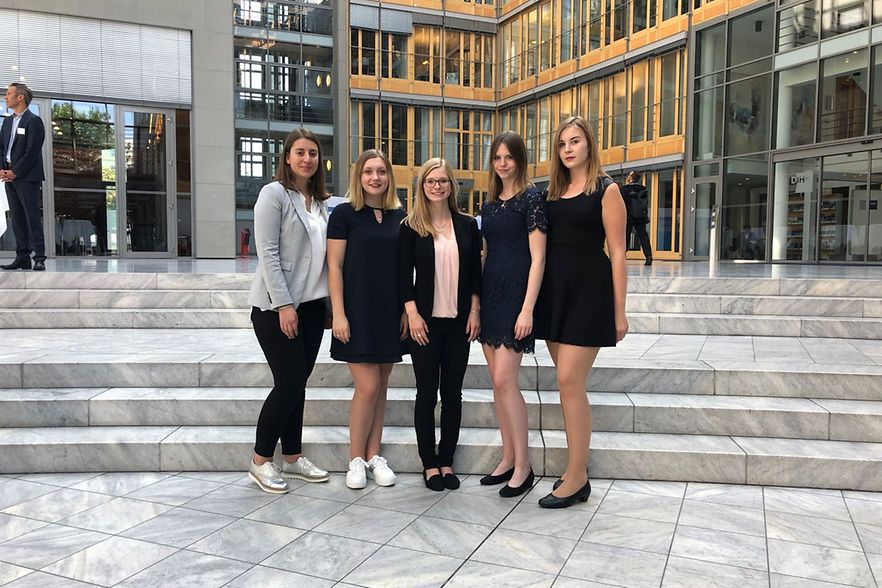 F&uuml;nf junge Frauen stehen f&uuml;r Gruppenfoto auf Marmortreppe in modernem Geb&auml;ude