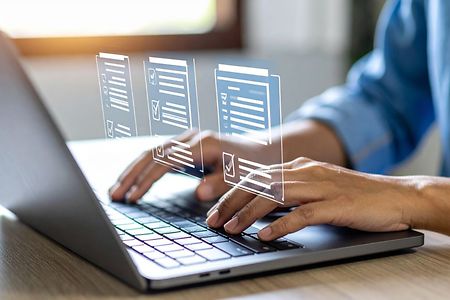 Person tippt auf einem Laptop, dar&uuml;ber schweben digitale Formulare als Symbole.