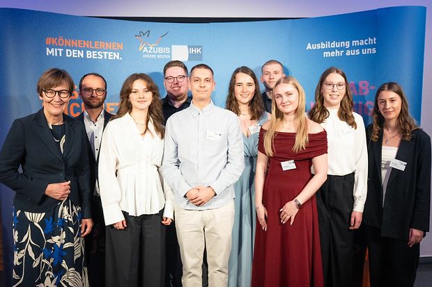Gruppenfoto von ausgezeichneten Auszubildenden und Vertretern der IHK vor einer Veranstaltungswand.