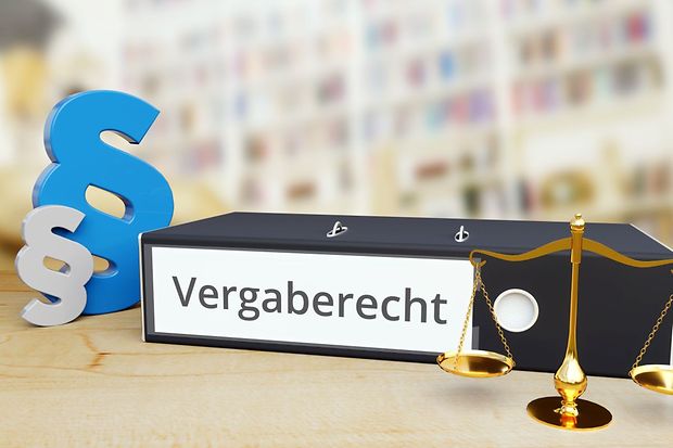 Ordner mit der Aufschrift &bdquo;Vergaberecht&ldquo;, daneben Paragrafenzeichen und eine Waage als Symbol f&uuml;r Recht und Vergabe.