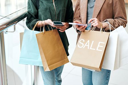 Hands of two young contemporary shoppers with smartphones and paperbags