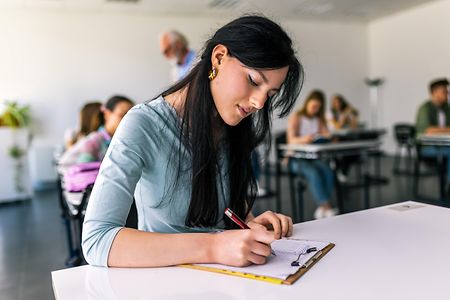 Focused young student taking notes from books for her study. College student sitting at desk and studying.