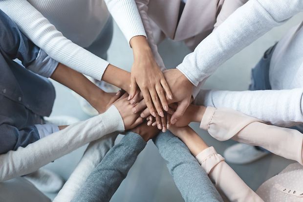 Mehrere H&auml;nde liegen &uuml;bereinander als Symbol f&uuml;r Teamwork und Zusammenhalt.