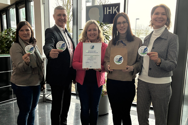 Gruppe mit Zertifikat und Siegeln im IHK‑Eingangsbereich