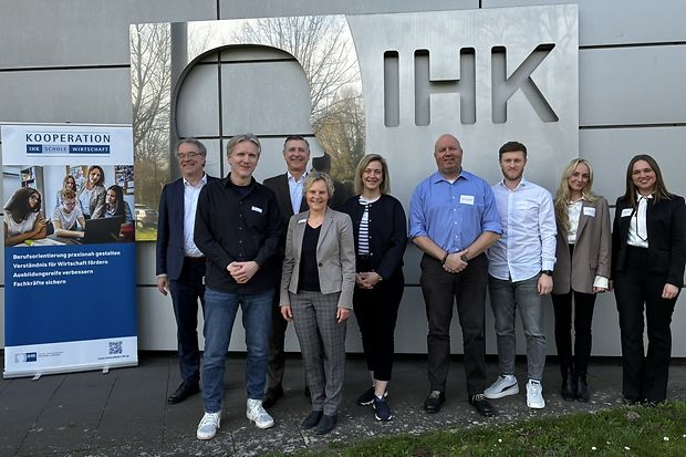 Gruppe mit neun Personen posiert vor IHK-Logo