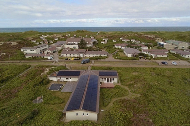 Luftaufnahme eines l&auml;nglichen Geb&auml;udes in den D&uuml;nen mit Photovoltaik