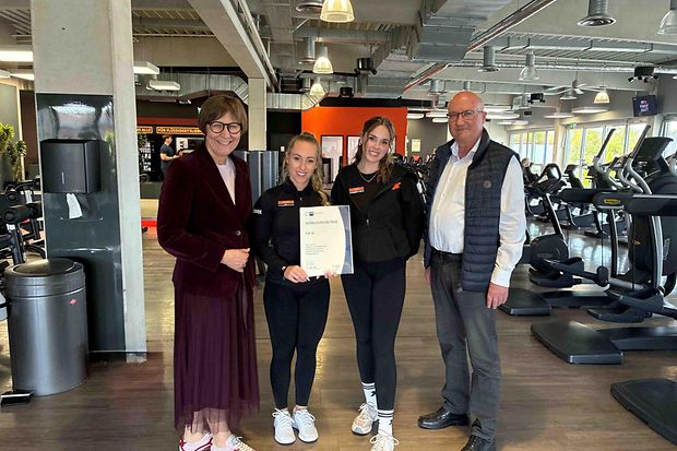 Vier Personen im Fitnessstudio, zwei halten ein Zertifikat