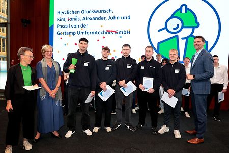Auszubildende bei einer Preisverleihung mit Urkunden und Troph&auml;e