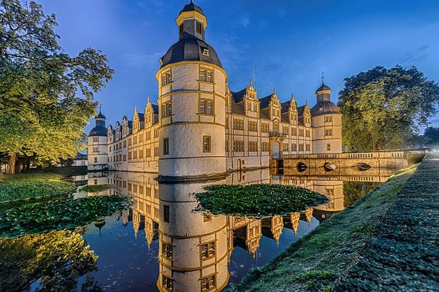 chloss Neuhaus mit Spiegelung im Wassergraben bei Abendd&auml;mmerung