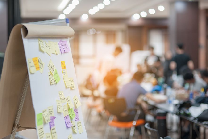 Blick in einen Besprechungsraum. Im Vordergrund steht ein Flipchart mit Post-it-Zetteln