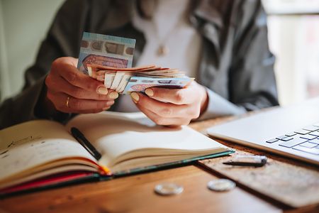 Eine Frau z&auml;hlt Euro-Scheine und macht ihre Buchf&uuml;hrung