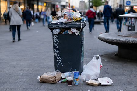 &Uuml;berf&uuml;llter M&uuml;lleimer mit Einwegverpackungen in einer Fu&szlig;g&auml;ngerzone