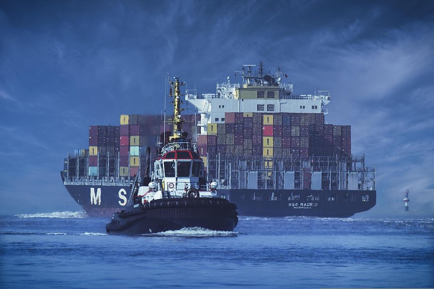 Schlepperboot vor einem gro&szlig;en Containerschiff auf dem Wasser, Symbolbild f&uuml;r internationale Schifffahrt