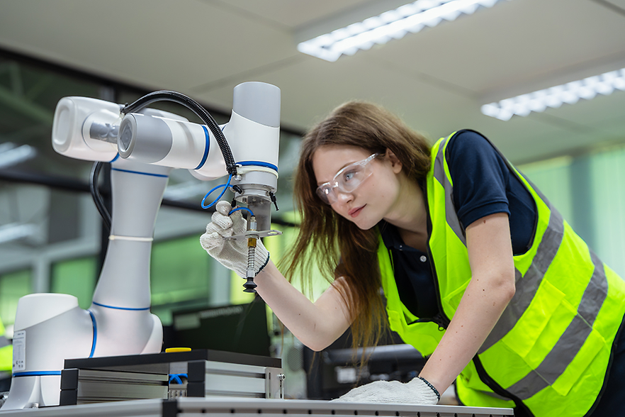 Weibliche Azubis werden an einem Industrieroboter ausgebildet