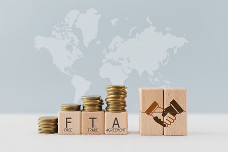 Freihandelsabkommen dargestellt durch M&uuml;nzstapel, Holzw&uuml;rfel mit &bdquo;FTA&ldquo; und ein Handschlag-Symbol.