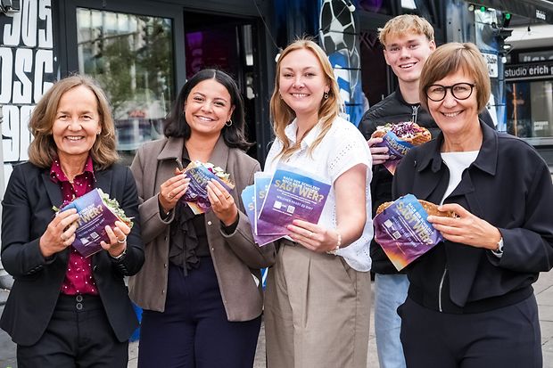 F&uuml;nf Menschen halten D&ouml;nert&uuml;ten und essen D&ouml;ner vor einem Gesch&auml;ft.