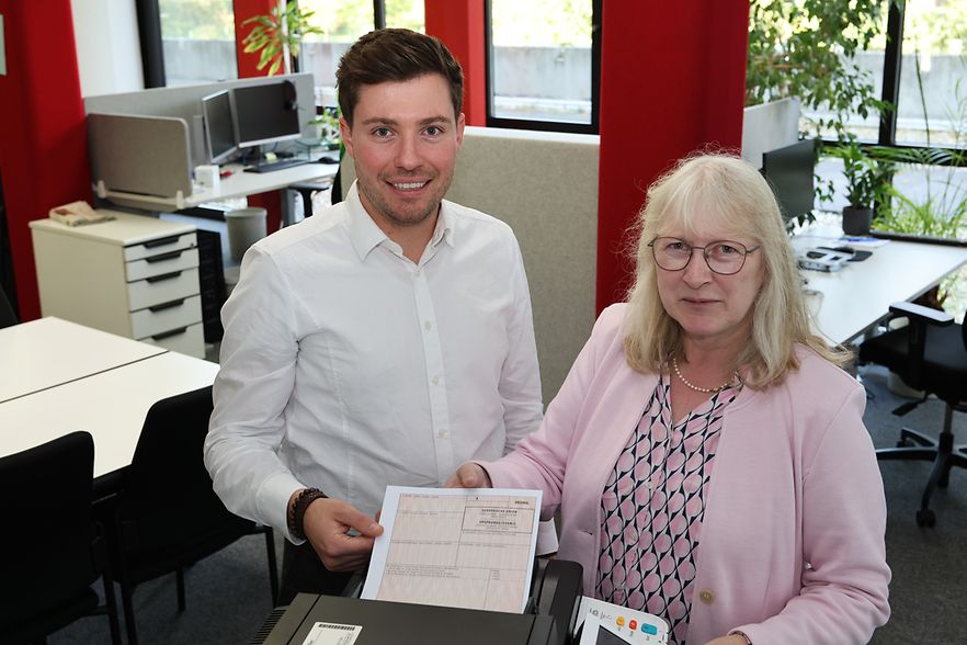 Eine Frau und ein Mann stehen vor einem Drucker mit einem Dokument